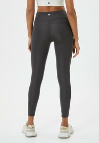 Leggings sportivi grigi a vita alta realizzati in materiale liscio ed elastico. Presentano cuciture piatte e un logo in vita.