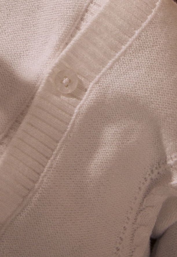 Gros plan d'un cardigan beige en maille montrant un col côtelé avec un bouton unique et des détails en tissu tricoté texturé.