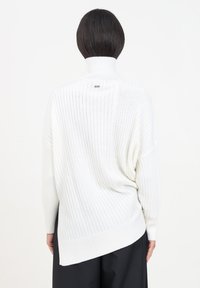 Maglione bianco a collo alto con texture a coste, dal collo alto e orlo con spacchi laterali. Texture morbida e vestibilità rilassata e oversize.