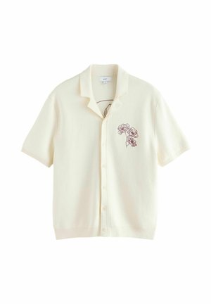 Krémová košile s krátkými rukávy na knoflíky, s otevřeným límcem a malou tmavou květinovou výšivkou na levé straně hrudi.