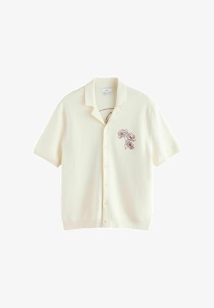 Kreemjas lühikeste varrukatega nööpidega särk avatud kraega ja väikese tumeda lillelist tikandiga vasakul rinnal.