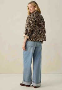Luipaardprint jasje met een ontspannen pasvorm, opgerolde mouwen, gecombineerd met lichtblauwe wijduitlopende jeans en bruine schoenen. Aardse kleurenpalet.