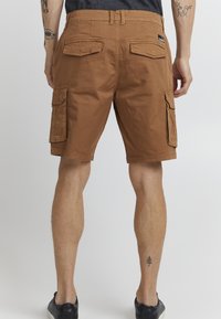 Brune bomull cargo shorts har side- og baklommer, en avslappet passform og oppbrettede kanter. Stoffet ser slitesterkt ut med en glatt tekstur.