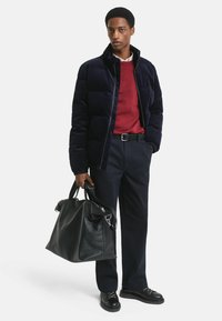 Marineblauer gestepptes Pufferjacke, roter Pullover, dunkle Hose, schwarze Lederhandtasche. Glatte Texturen, strukturierte Designs, minimale Akzente und robuste Schuhe.