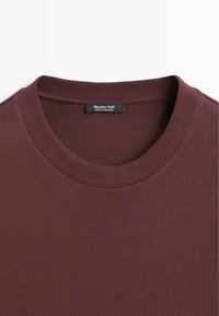 Burgundowy sweter z okrągłym dekoltem wykonany z miękkiego materiału, z prążkowanym kołnierzem i metką oznaczoną "Massimo Dutti Made in Portugal."