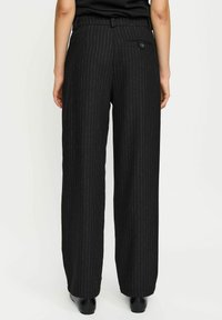 Zwarte broek met streepjes in een wijd model. Voorzien van een achterzak met knoop, gemaakt van een gestructureerde stof met een gladde textuur.