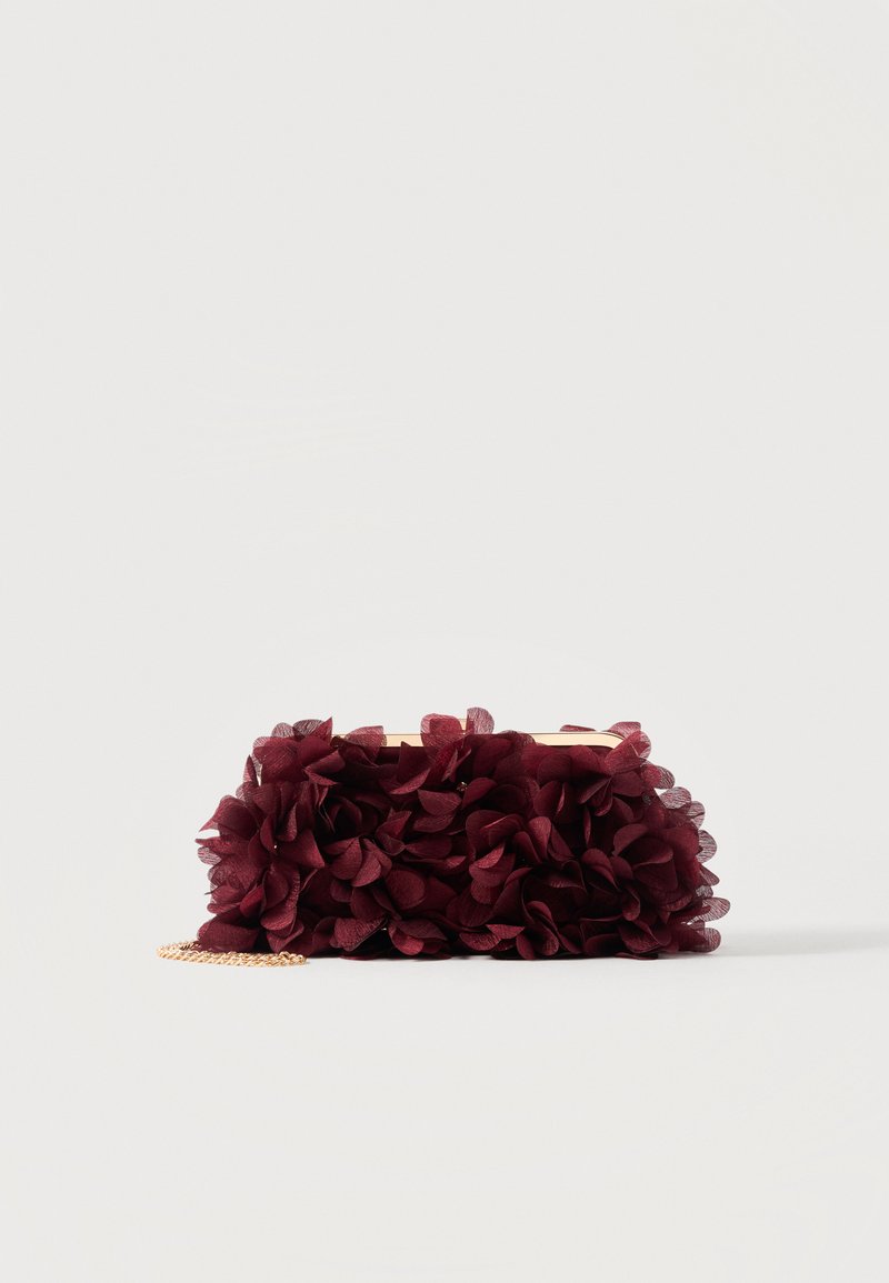 Pochette recouverte de pétales en tissu bordeaux avec un cadre métallique doré et une courte bandoulière chaîne dorée, présentée sur un fond uni.
