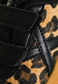 Sneaker in pelle nera con punta e pannelli laterali a stampa leopardata, dotato di cinturini in velcro e dettagli testurizzati per una presa migliore.
