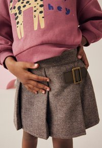 Falda de espiga gris con un detalle de cinturón de hebilla marrón, combinada con una sudadera rosa con un diseño de leopardo y texto gráfico.