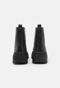 Botas de cuero negro hasta el tobillo con una suela gruesa, que presentan líneas elegantes, una textura suave y tiradores traseros para ponerlas con facilidad.
