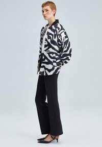 Jakna s črno-belo zebraste vzorcem z ovratnikom, v kombinaciji s črnimi širokimi hlačami in čevlji s koničastim nosom. Gladko blago z strukturiranimi detajli.