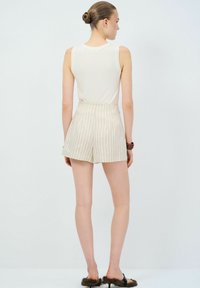 Top senza maniche beige chiaro e pantaloni corti a righe con vita alta e vestibilità ampia. L'outfit presenta una texture liscia e un design minimalista.