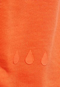 Ljust orange tyg med ribbad textur har tre små, stiliserade applikationer i form av vattendroppar i matchande färg.