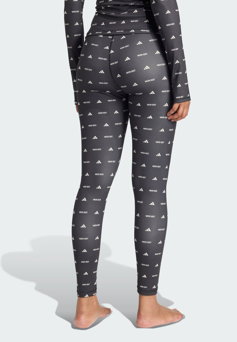 Leggings negros hechos de una tela elástica, con un patrón de logotipos blancos repetido. Diseño ajustado sin hardware o acentos visibles.