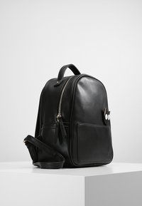 Czarny skórzany plecak o zaokrąglonym kształcie, z złotym zamkiem błyskawicznym, przednią kieszenią oraz zabawnym wzorem kota z okrągłymi oczami i uszami.