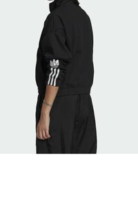 Black sweatshirt with high collar, white three-stripe accents on sleeves, and embroidered logo on left arm. Soft, textured fabric.