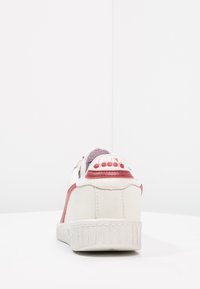 Sneaker bianco in pelle con dettagli rosa, suola in gomma testurizzata, punta rotonda, design con lacci e branding sul tallone.