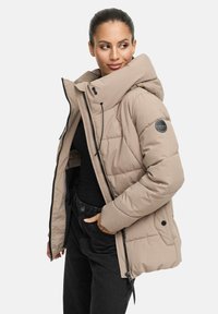 Beige pufferjack met een grote capuchon, zwarte rits en trekkoorddetails. Kenmerkt zich door een gewatteerd patroon en een ronde logo op de mouw.