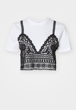 T-shirt blanc à manches courtes avec un superposition en dentelle noire présentant des motifs floraux complexes et un design court. Des bretelles noires s'étendent du haut.