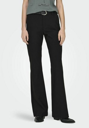 Pantaloni neri a palazzo con una texture liscia, dotati di passanti per cintura con una fibbia d'argento, abbinati a una camicia grigia. Scarpe nere con suola piatta.