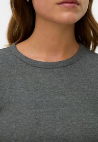 Gros plan sur le bas du visage et le cou d'une femme portant un pull gris  à col rond côtelé.