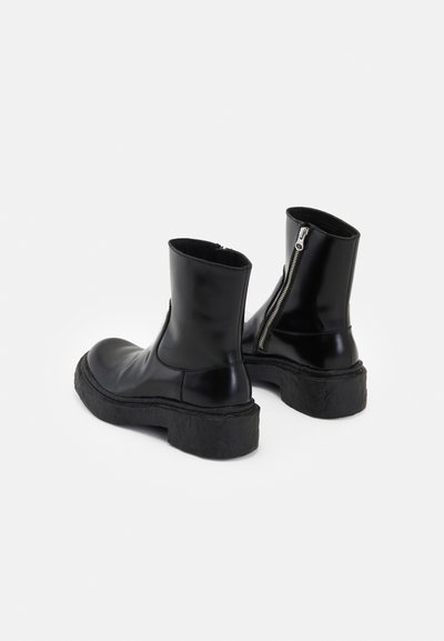 Botas de tobillo de cuero negro con suela de goma texturizada, cierre de cremallera lateral y acabado suave. Diseño simple con forma de punta redondeada.
