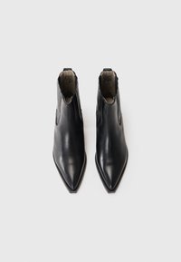 Botas de tobillo de cuero negro con punta afilada, que presentan una textura suave y aberturas laterales para facilitar el uso. Diseño minimalista sin adornos.