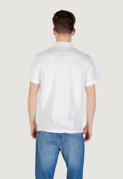 Polo shirt blanc à manches courtes avec un col classique, associé à un jean en denim bleu clair. Le tissu semble lisse et légèrement texturé.