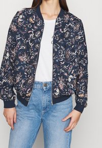 Blommig bomberjacka i marinblått med intrikata flerfärgade mönster. Har dragkedja framtill, ribbad mudd och midjeband. Kombineras med ljusblå denim.