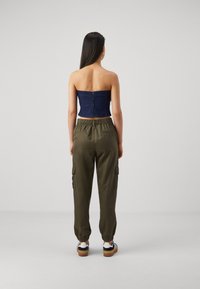 Denim bešvarko viršus su lygiu paviršiumi ir užtrauktuku nugaroje, derinamas su alyvuogių žalios spalvos cargo kelnėmis, turinčiomis elastingus rankogalius ir šonines kišenes.