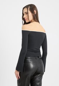 Schwarz off-shoulder Langarmtop mit weißem Saum, verfügt über eine taillierte Passform und glatte Textur, kombiniert mit hochtaillierten, fauxledernen Hosen.
