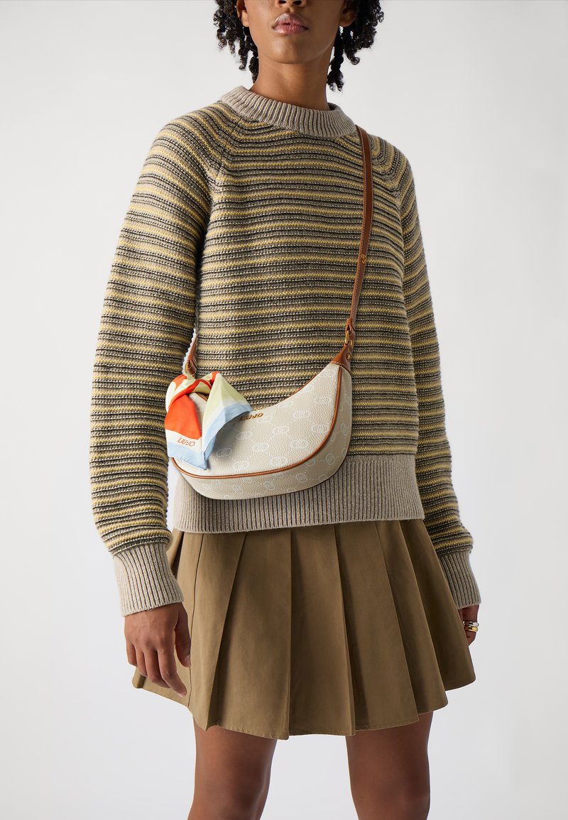 Pequeño bolso de crema con un patrón de logo, forma curvada, correa de cuero marrón y una bufanda de seda multicolor atada en la parte delantera.