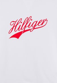 Sudadera blanca con un gran logotipo en cursiva roja, "Hilfiger," centrado en la parte delantera. Textura suave con un diseño de ajuste clásico.