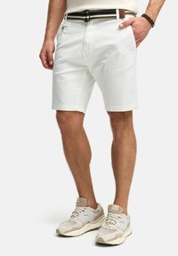 White cotton shorts with a straight fit, belt loops, and side pockets. Paired with beige athletic sneakers featuring gray accents.
