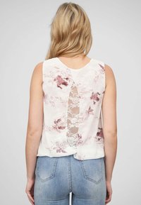 Blouse florale avec une base blanche et des fleurs roses, un détail en dentelle dans le dos et une coupe décontractée. Associée à un jean bleu clair.