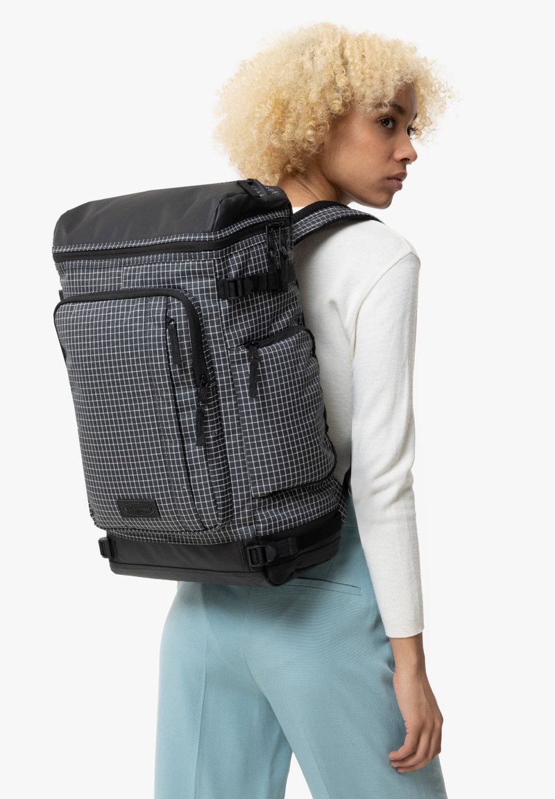 Zaino in tessuto a scacchi grigi e neri con molteplici tasche con zip, maniglia superiore e spallacci regolabili. Tessuto testurizzato con finitura opaca.
