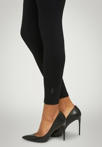 Leggings neri a coste abbinati a eleganti tacchi a spillo neri, con punta appuntita e texture lucida, che mostrano un design minimalista.