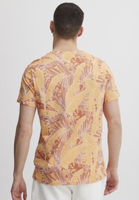 Camiseta de manga corta en color naranja con un patrón de hojas tropicales, con contornos blancos y una tela suave y ligera.