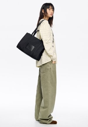 Czarna torba na ramię z podwójnymi paskami i prostokątnym kształtem. Posiada teksturowaną naszywkę z logo oraz gładką powierzchnię materiału.