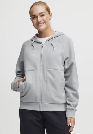 Sweatshirt à capuche zippé gris en matériau doux, avec une capuche doublée, des poches avant et des bords côtes, présentant une texture lisse et une coupe décontractée.