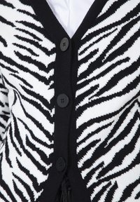 Cardigan a righe zebrate in bianco e nero con tre bottoni neri sopra una camicia o top bianco.