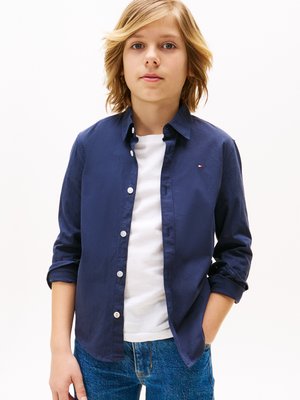 Mørkeblå knappet skjorte, lett stoff, lange ermer rullet opp litt, brukt over en hvit T-skjorte, kombinert med blå jeans.