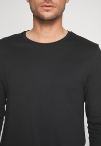 Cămașă neagră cu mânecă lungă și guler rotund. Confecționată dintr-un material neted și ușor. Prezintă o formă ajustată și detalii de cusătură minime.
