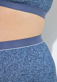 Modrý sportovní set s texturovaným vzorem v různých odstínech. Pas je v jednotné modré barvě s kontrastním bílým pruhováním.