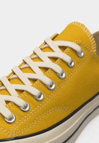 Baskets en toile jaune avec des lacets blancs passés dans des œillets métalliques et une semelle en caoutchouc blanche bordée de noir.