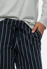 Marine gestreepte broek van zachte stof, met een elastische tailleband en een strikkoord, en met zijzakken. Een bijpassend grijs topje is gedeeltelijk zichtbaar.