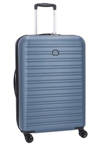 Valigia rigida blu con striature orizzontali, manico telescopico, quattro ruote nere e un logo arrotondato sulla parte frontale. Superficie liscia.