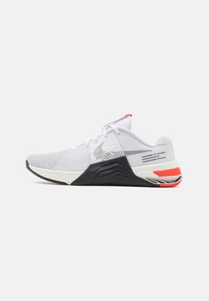 Witte sportieve schoen van ademend mesh met een textuur bovenwerk, zwarte duurzame zool en rode en oranje accenten op de hiel.
