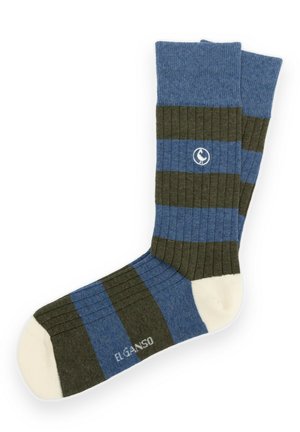 Un par de calcetines de media caña a rayas azules y verde oscuro, con punteras de color crema y un pequeño emblema blanco, sobre un fondo blanco.
