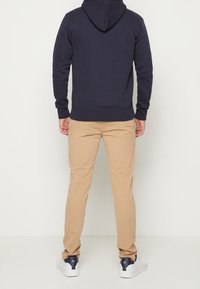 Sudadera azul marino con cordón y mangas largas, combinada con pantalones chinos beige y zapatillas blancas con detalles en azul marino oscuro en el talón.